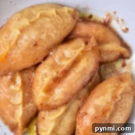 A plate with six golden-brown sweet potato dumplings rests on a pristine white surface, ready to be enjoyed.