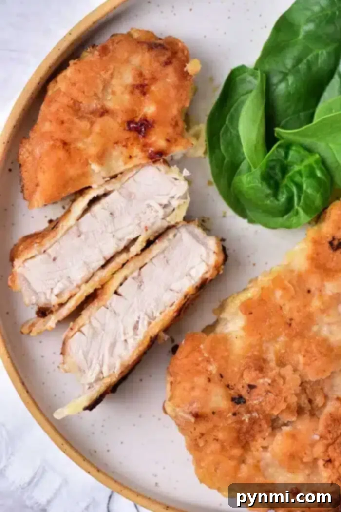 Tenderized Pork Cutlets 2 A plate featuring breaded and fried pork cube steaks, with one chop sliced to show the tender interior. Fresh spinach leaves are placed beside the chops on the light-colored plate.