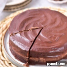 Chocolate coffee cake with a shiny ganache frosting and one slice cut out, resting on a woven placemat.