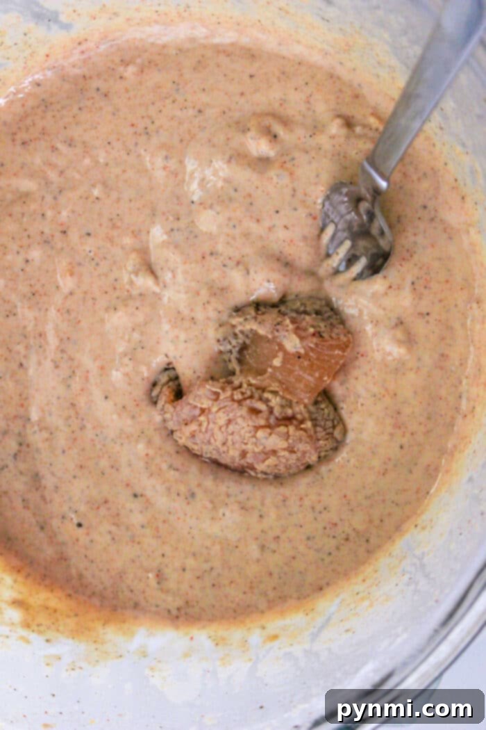 Close-up of a glass bowl filled with tempura batter, a fork stirring the mixture, ready to coat the chicken nuggets.