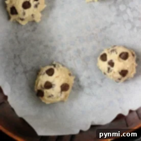 Air Fryer Cookie Dough Delights 4 Four air fryer cookie dough balls arranged on a parchment-lined baking sheet. The dough balls are spaced apart, ready for baking.