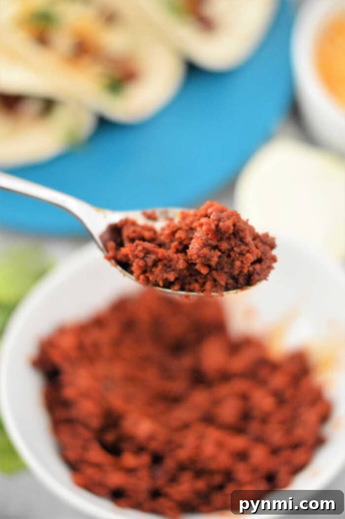 Close-up of a spoonful of seasoned chorizo over a bowl, highlighting the delicious textures and flavors of a chorizo taco recipe, with blurred tacos in the background.