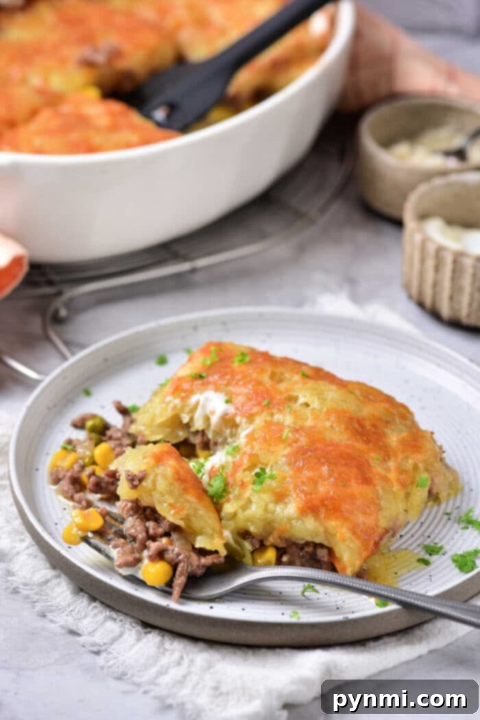 Hearty Beef and Hash Brown Bake 6 A perfect slice of ground beef hash brown casserole with melted cheese and visible vegetables, serving dish in the background.