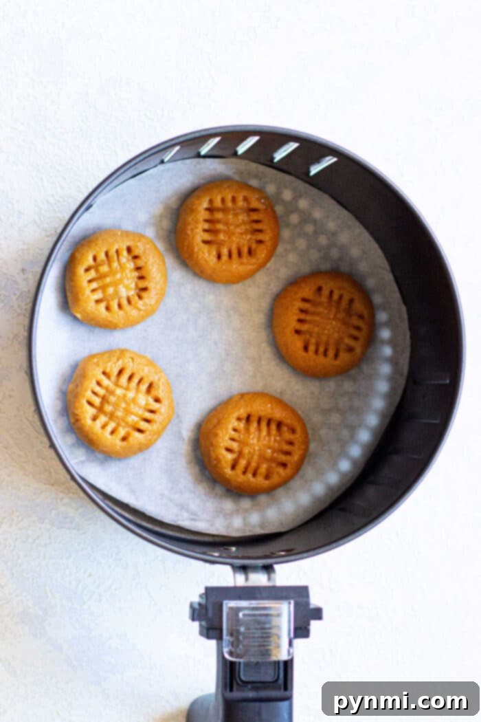 Golden Air Fryer Peanut Butter Delights 4 Four air fryer peanut butter cookies cooling in the air fryer basket on a piece of parchment paper.