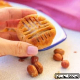 Hand holding an air fryer peanut butter cookie with a classic fork design, surrounded by peanuts on a light surface.