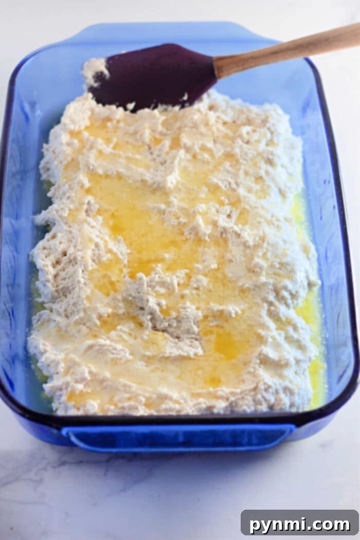 Blue baking dish with bisquick biscuit batter and melted butter, being spread with a spatula to create easy 4 Ingredients Basic Biscuits.