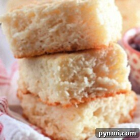 Two stacked fluffy butter swim biscuits, made from just 4 ingredients, rest on a white cloth with a blurred backdrop of jam.