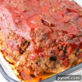 A freshly baked spicy meatloaf in a glass dish, topped with zesty tomato sauce.