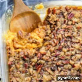 A glass dish with a delectable sweet potato casserole recipe featuring canned yams, topped with crunchy pecans and accompanied by a wooden spoon.