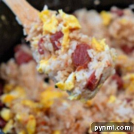 A close-up of a spoonful of Chinese Sausage Fried Rice reveals perfectly scrambled eggs mingling with slices of savory sausage over a sizzling pan.