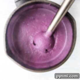 A blender effortlessly transforms ingredients into a vibrant purple pureed soup, swirling smoothly in the pot on a light surface.