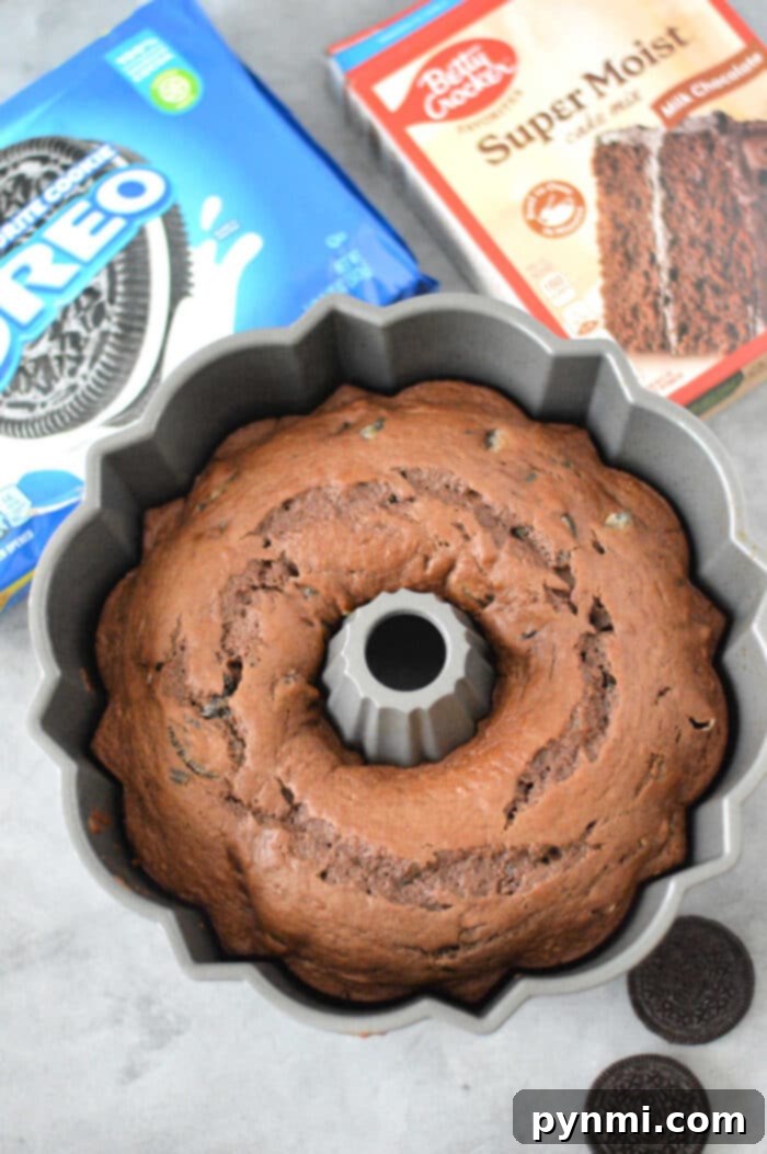 An Oreo cake made with cake mix, prepared in a bundt pan and surrounded by extra Oreos and cake mix boxes on a rustic gray surface, symbolizing ease and deliciousness.
