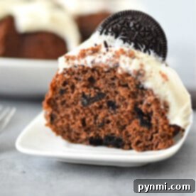 A slice of Oreo Bundt Cake sits elegantly on a white plate, crowned with white frosting and garnished with a classic Oreo cookie.