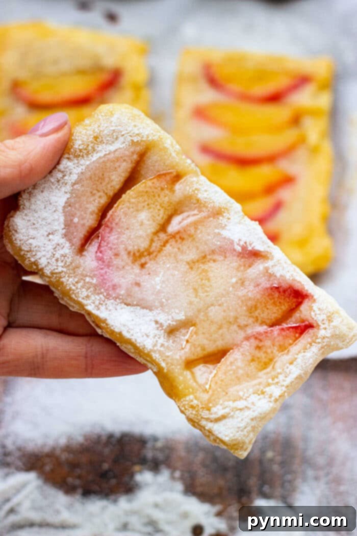 Golden Peach Delight 2 Golden-brown peach puff pastry desserts on a baking sheet, garnished with powdered sugar and fresh mint, ready to be served.