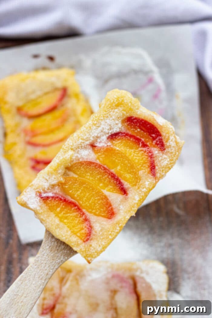 Golden Peach Delight 7 Two golden-brown peach puff pastry tarts on a rustic wooden board, garnished with powdered sugar and fresh mint leaves, with more pastries blurred in the background.