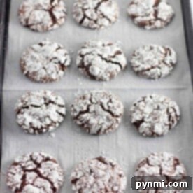A tray of twelve Cool Whip chocolate crinkle cookies dusted with powdered sugar rests on parchment paper.