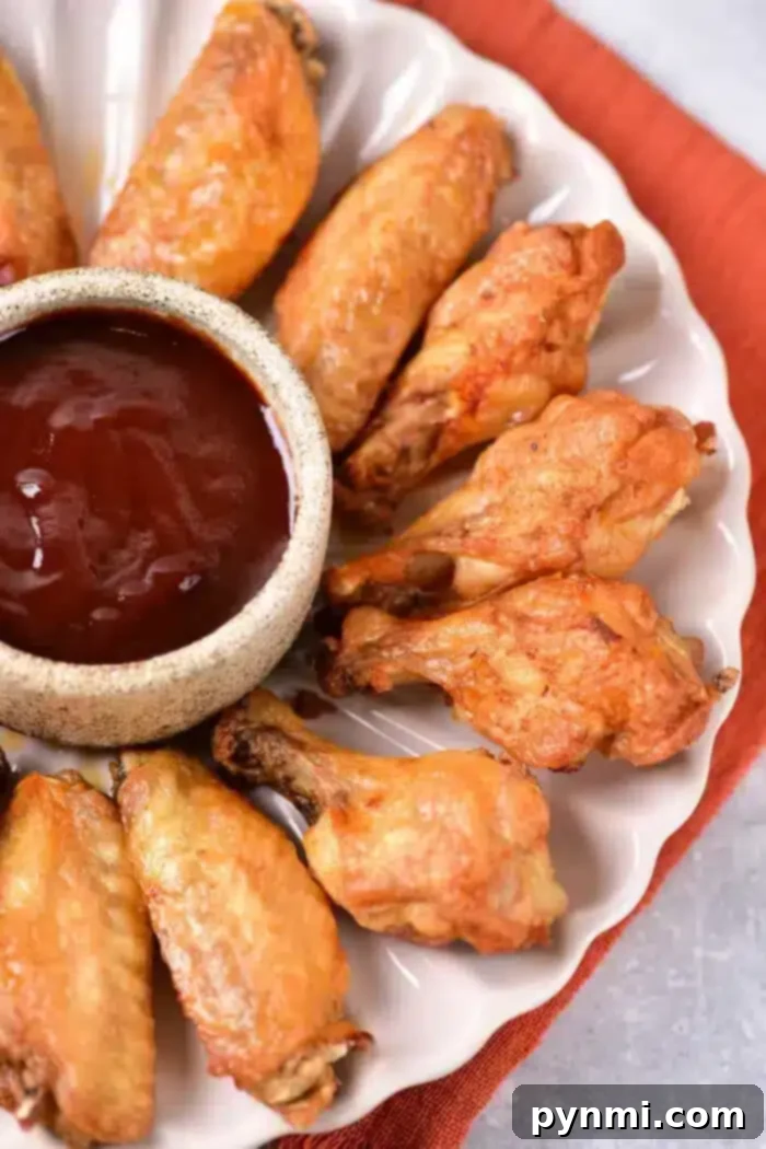 Poached Chicken Wings 6 A plate of golden-brown, boiled chicken wings is arranged in a circular pattern around a small bowl filled with dark barbecue sauce. The plate rests elegantly on an orange cloth.