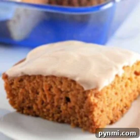 A slice of frosted pumpkin cake, reminiscent of a classic Crazy Cake, rests on a white plate with a vibrant blue dish in the background.