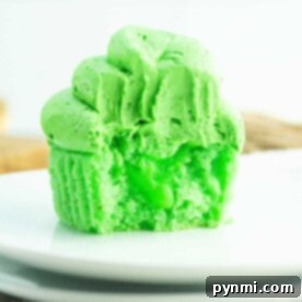 A vibrant green cupcake with frosting rests elegantly on a white plate, delighting those with a penchant for green cupcakes.