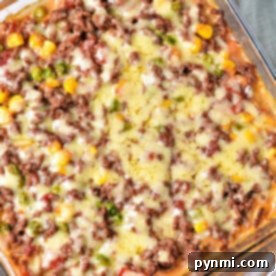 The ShipWreck Casserole is a delightful baked dish featuring ground meat, melted cheese, corn, peas, and tomatoes all layered beautifully in a square glass dish.