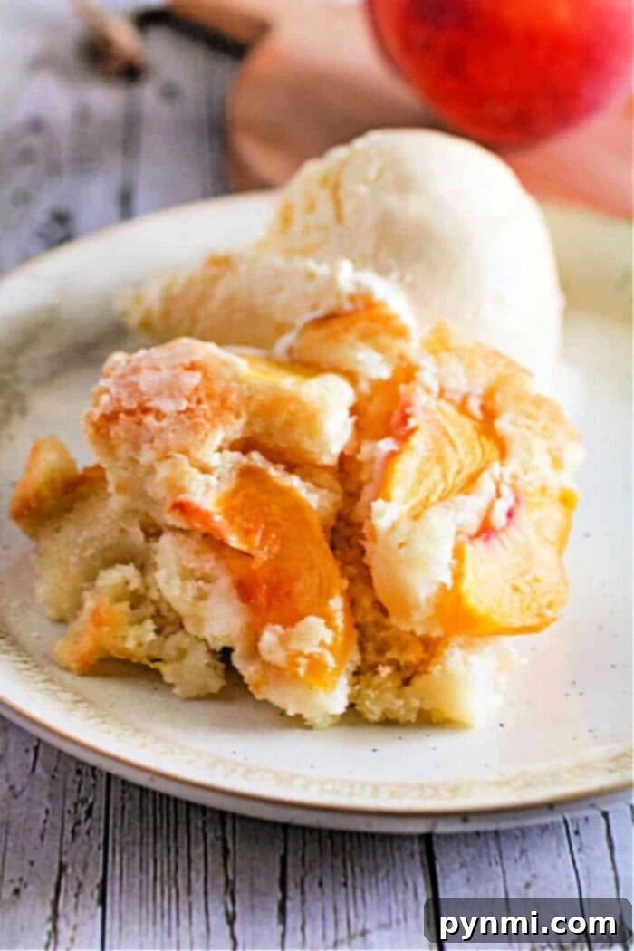A slice of golden brown fresh peach dump cake, topped with a melting scoop of vanilla ice cream, sits on a white plate, ready to be enjoyed.