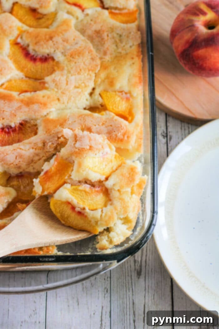 A slice of warm peach cobbler cake on a white plate, showcasing the fluffy cake and juicy peaches.