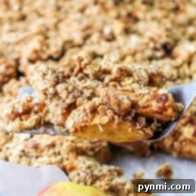 Warm Cinnamon Apple Slices 7 A spatula holds a freshly baked apple crumble piece, the perfect showcase for your apple slices recipe, with a whole apple in the foreground.