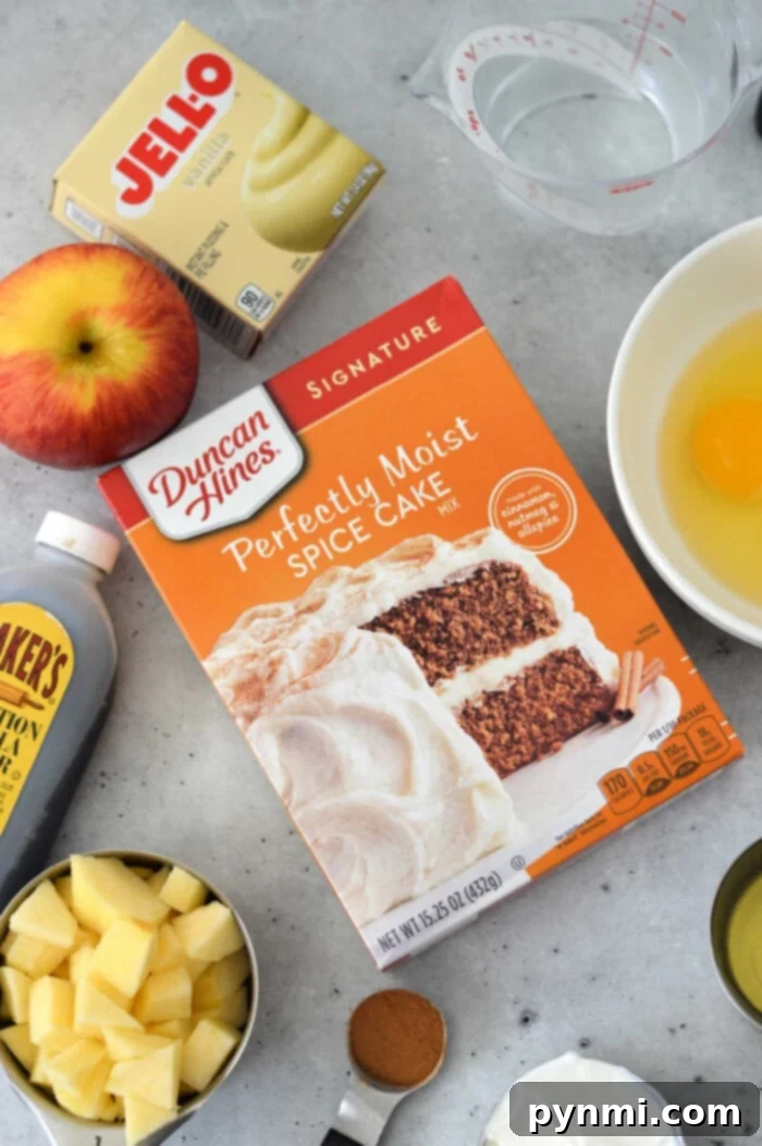 Quick Cake Mix Apple Delight 2 An array of tempting ingredients awaits on the kitchen counter: a box for Apple Cake with Cake Mix, creamy pudding, aromatic cinnamon, chopped apples, an egg, golden syrup, and a trusty measuring cup to tie it all together.
