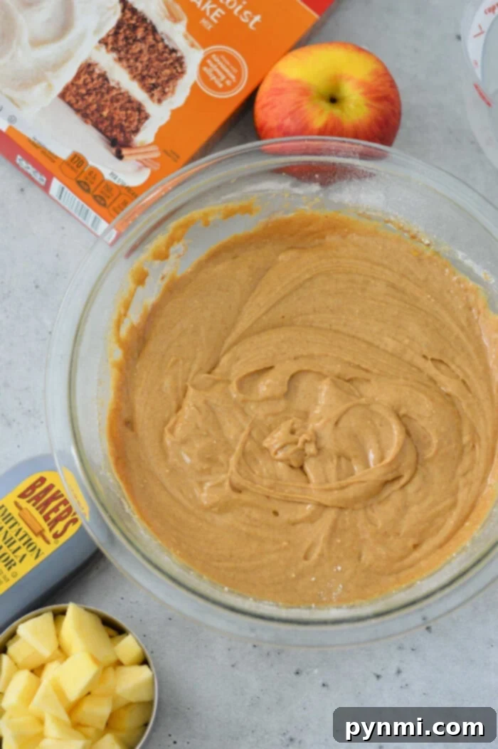 Quick Cake Mix Apple Delight 3 A glass bowl filled with cake batter sits gracefully on the countertop, surrounded by a box of cake mix, chopped apples, a whole apple, and a measuring cup—perfect ingredients for an effortless apple cake.