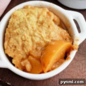 A delicious crockpot peach cobbler with cake mix, served beautifully in a small white dish on a wooden surface.