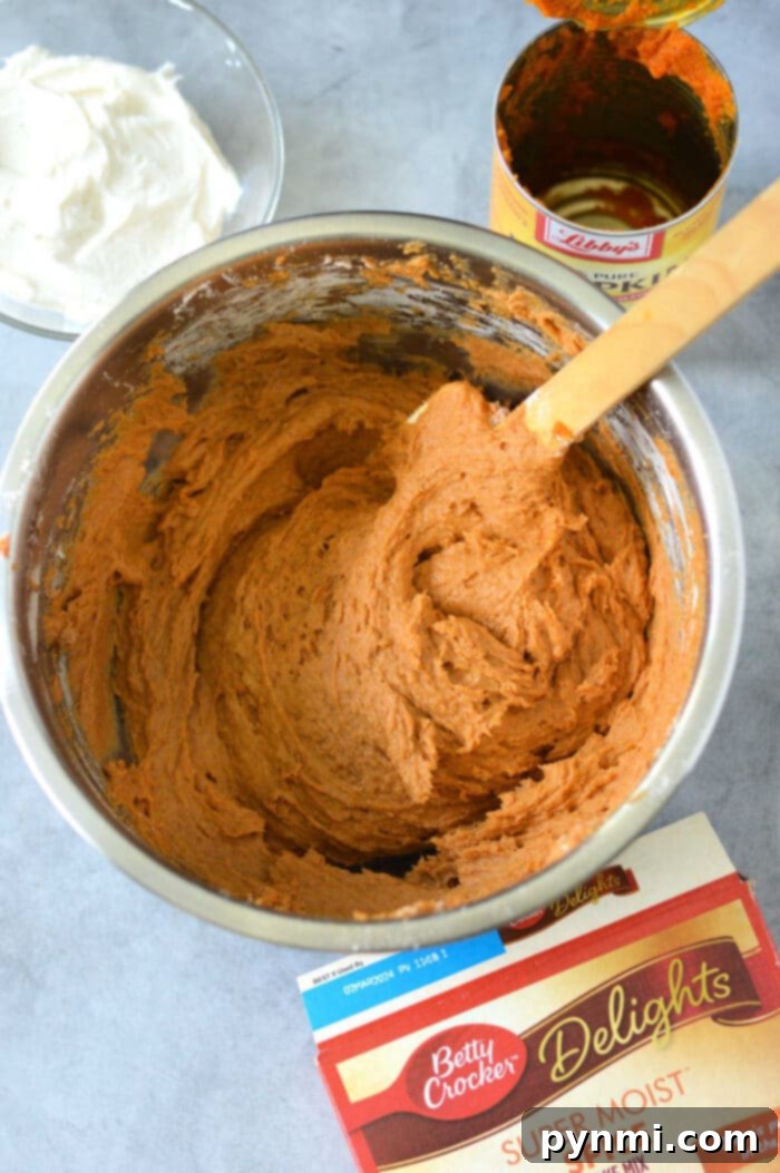 Effortless Pumpkin Spice Cake Mix Bars 4 A mixing bowl filled with pumpkin cake bars batter sits on a gray surface, surrounded by canned pumpkin and a cake mix box, ready to whip up delicious pumpkin bars with cake mix. Nearby, whipped topping waits to add the finishing touch.