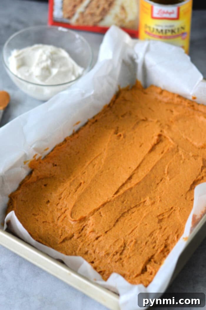 Effortless Pumpkin Spice Cake Mix Bars 5 A freshly baked batch of Libby's Pumpkin Bars, frosted and ready to be sliced, presented on a wooden surface.