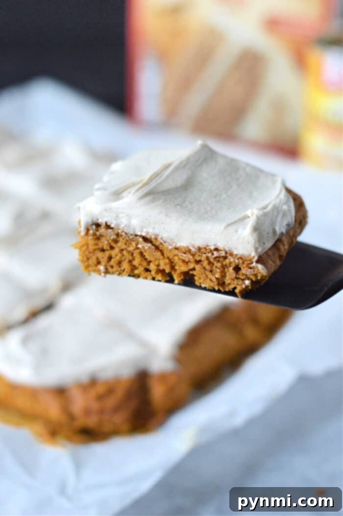 Effortless Pumpkin Spice Cake Mix Bars 6 A perfectly frosted square pumpkin bar with cake mix is carefully lifted on a spatula, showcasing its moist texture, with more delectable slices arranged on parchment paper below.