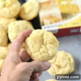 A hand holding a delectable cookie, with more cake mix cookies with cream cheese and a cake mix box in the background.