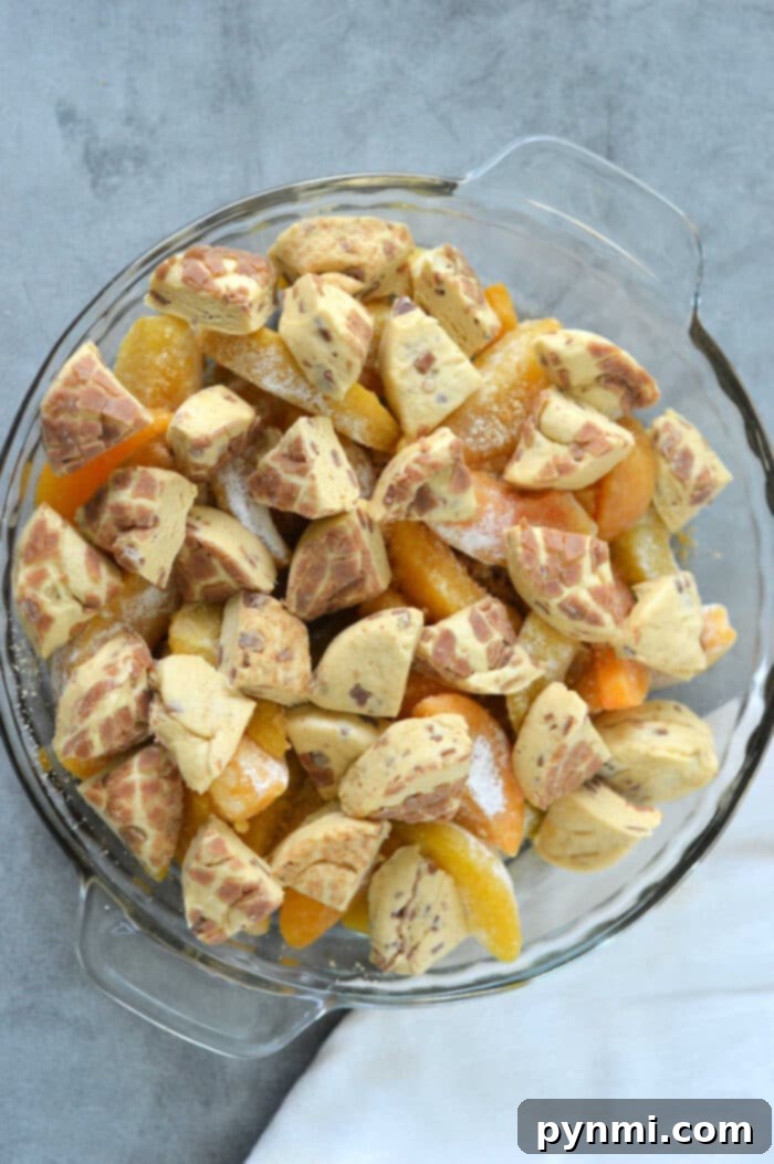 Peachy Cinnamon Swirl Cobbler 5 A glass dish brimming with peach slices, chunks of cinnamon rolls, and the warm embrace of cinnamon roll accents create a delightful cobbler experience.