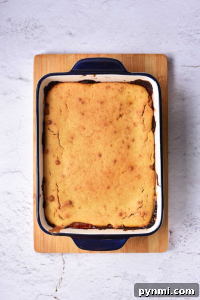 A freshly baked pear cake, golden-brown and steaming gently, presented in a rectangular blue and white baking dish on a rustic wooden board, ready to be served.