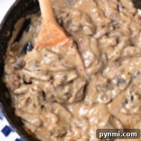 A pan of creamy, dairy-free mushroom sauce for beef stroganoff sits invitingly with a wooden spoon on a striped towel.