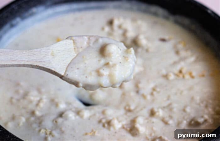 Pillowy Vegan Biscuits with Savory Gravy 5 A close-up of creamy vegan gravy in a pot, with a wooden spoon lifting a portion, evokes the comfort of enjoying vegan biscuits and gravy on a cozy morning.