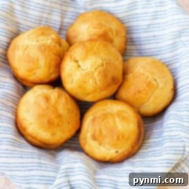 Golden-brown mayonnaise biscuits rest in a striped cloth-lined basket on a light textured surface.