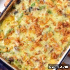 Cheesy Green Bean Casserole baked to perfection with melted cheese and crispy onions, served in a rectangular blue dish on a wooden trivet.