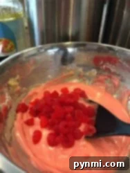 Sweet Cherry Loaf 5 A bowl of pink Maraschino Cherry Bread batter with chopped red cherries being mixed with a black spatula.