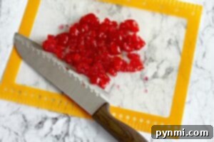Sweet Cherry Loaf 6 Chopped red candied cherries, perfect for Maraschino Cherry Bread, are spread on a cutting mat with a knife on a marble countertop.