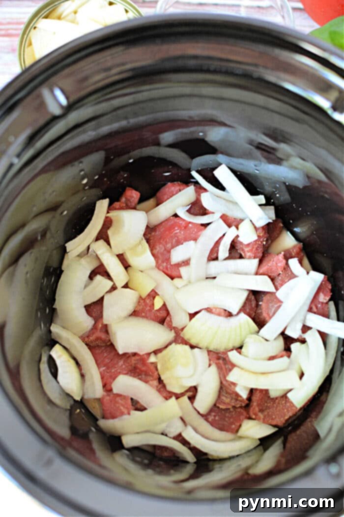 A close-up of Crockpot Pepper Steak, showing beef, onions, and colorful bell peppers simmering in a rich sauce