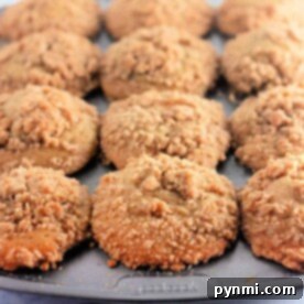 A muffin tray filled with crumb-topped peach cobbler muffins on a light background.