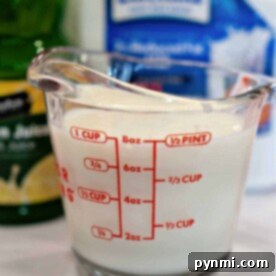 A measuring cup filled with milk, the first step in how to make buttermilk with lemon juice, stands surrounded by zesty lemon juice and milk carton containers.