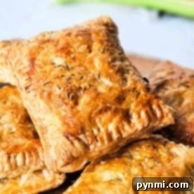 Golden, flaky puff pastry squares reminiscent of classic Hand Meat Pies, sprinkled with herbs and stacked on a wooden surface.