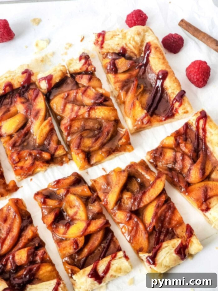 Puff Pastry Fruit Tart, a golden-brown tart with sliced peaches on top, garnished with fresh raspberries and a light drizzle.