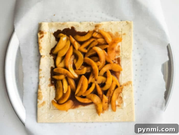 Peaches and puff pastry prepared for baking, showing the fruit arranged on the pastry.