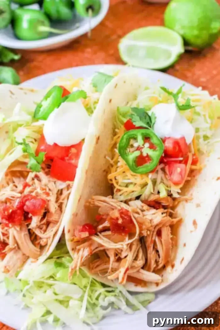 Kickin Rotel Tacos 7 Two Rotel tacos filled with shredded chicken, diced tomatoes, shredded cheese, jalapeño slices, sour cream, and lettuce on a white plate. A halved lime and extra jalapeños are in the background.