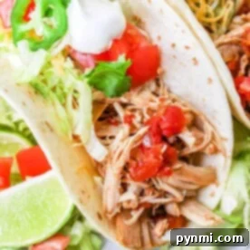 Two Rotel tacos loaded with shredded chicken, fresh lettuce, juicy tomato, creamy sour cream, fiery jalapeños, and zesty lime wedges on the side.